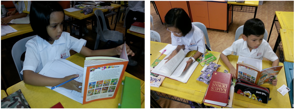 Three children in white uniforms sit at yellow desks reading and writing books in a classroom.